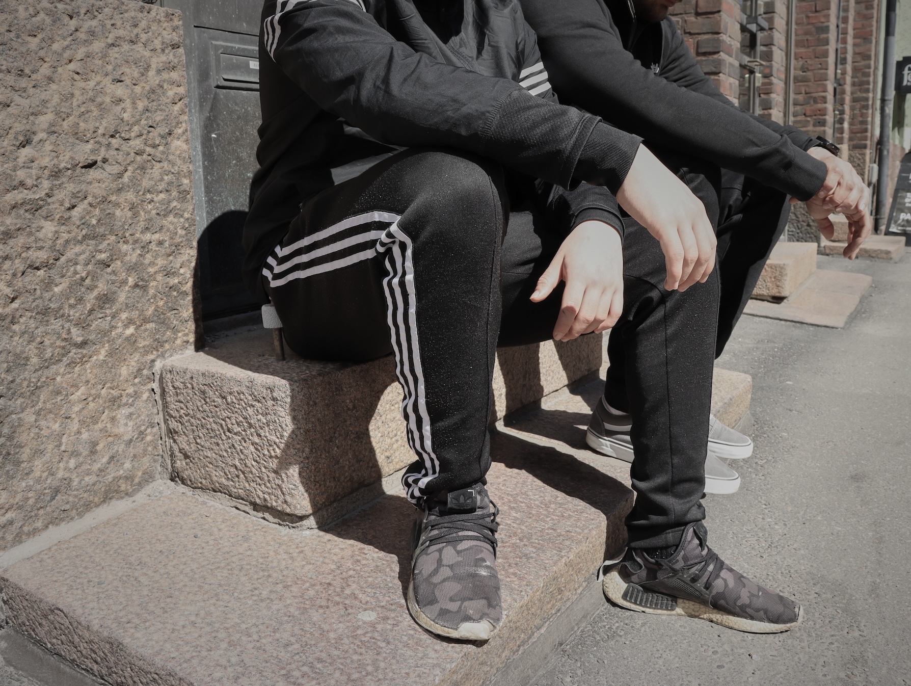 Kaksi henkilöä istuu portaalla ulkona, päät on rajattu pois kuvasta.