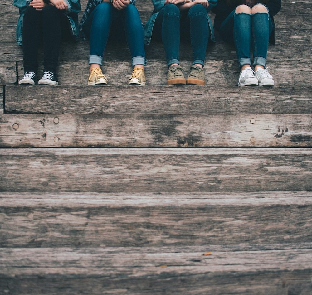 Neljä ihmistä istuu portailla, kuvassa näkyvät vain jalat.