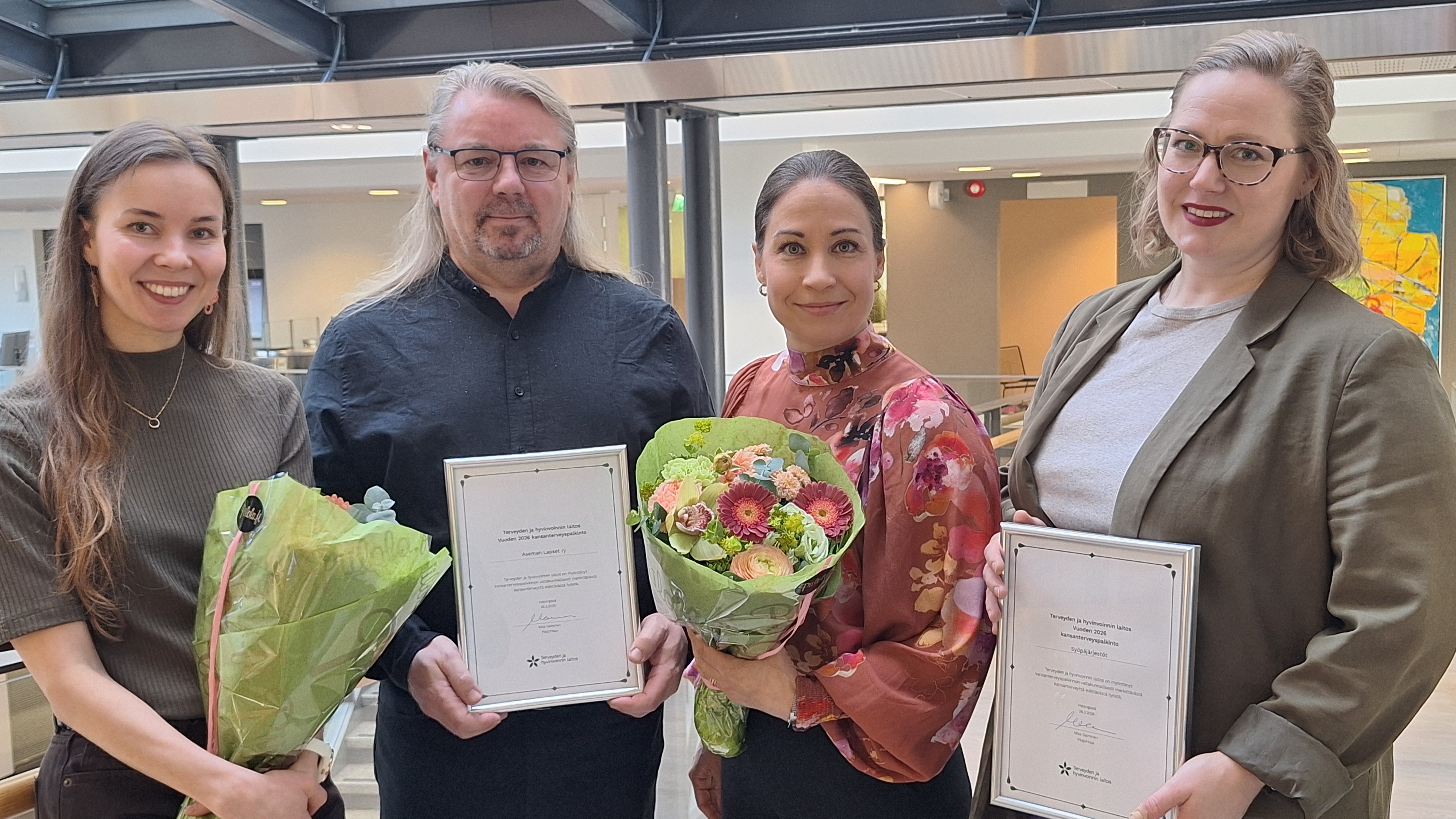 Neljä palkittua aikuista kukkien ja kunniakirjojen kanssa